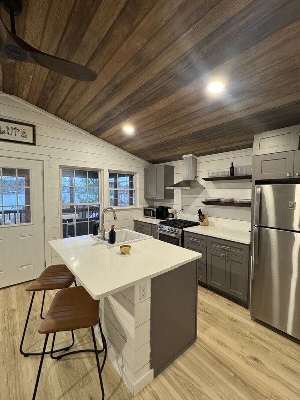 A modern kitchen with a central island, stainless steel appliances, and wooden ceiling.