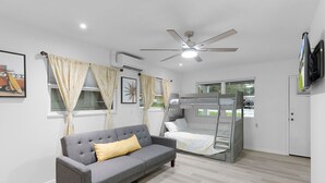 A room with a grey sofa, a bed with a canopy, a ceiling fan, and a television mounted on the wall. - Family-Friendly  sleeps 7-Home Close to Fun (Belleview)