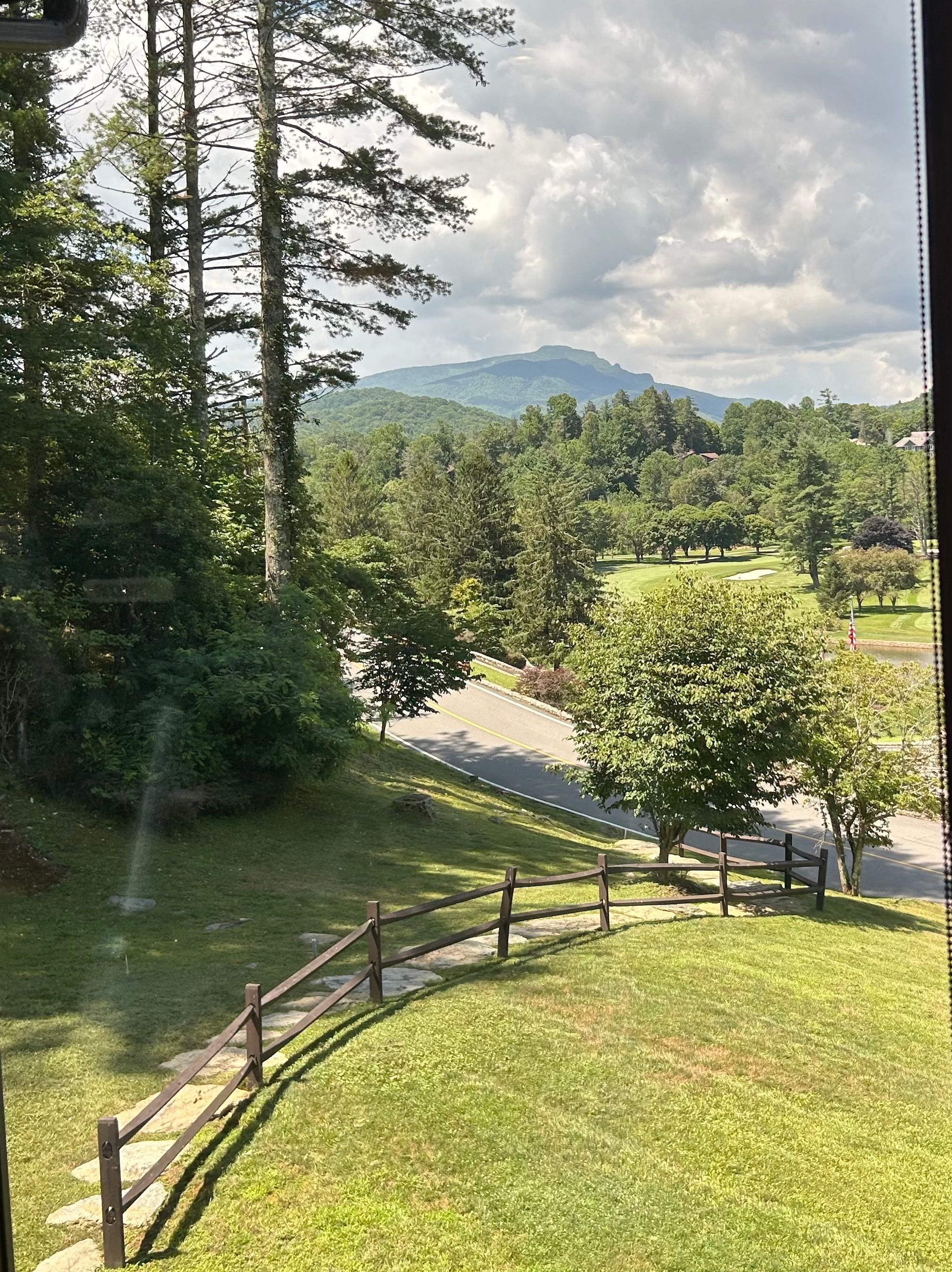 A view of a lush green landscape with a road, a wooden fence, and a mountain in the distance.