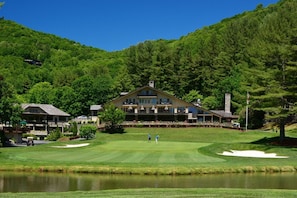 Ein Golfplatz mit Clubhaus, Teich und Bergkulisse im Hintergrund.