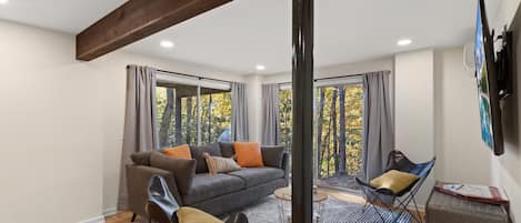 A modern living room with a sofa, two chairs, a coffee table, and large windows with curtains.