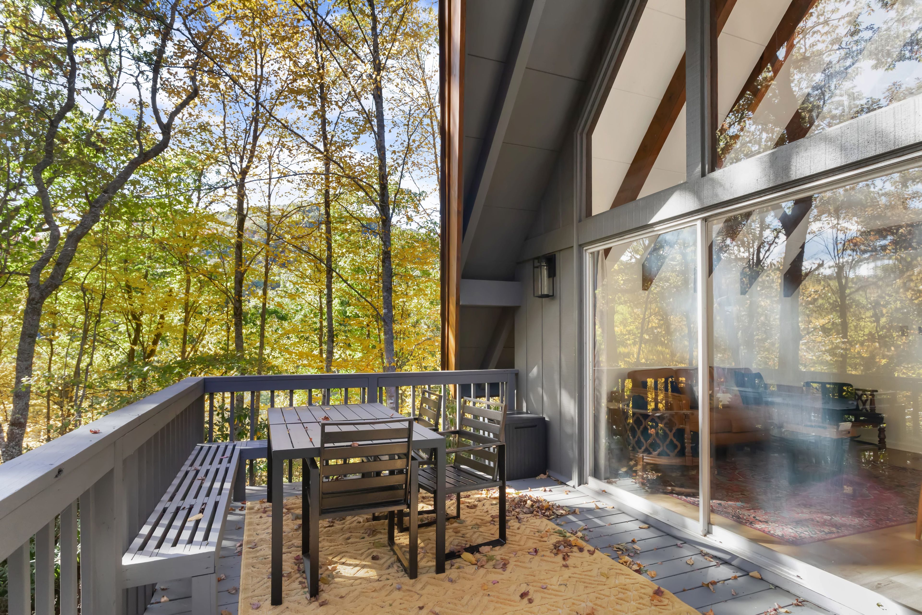 Una terraza de madera con una mesa y sillas, con vistas a un bosque con follaje otoñal.