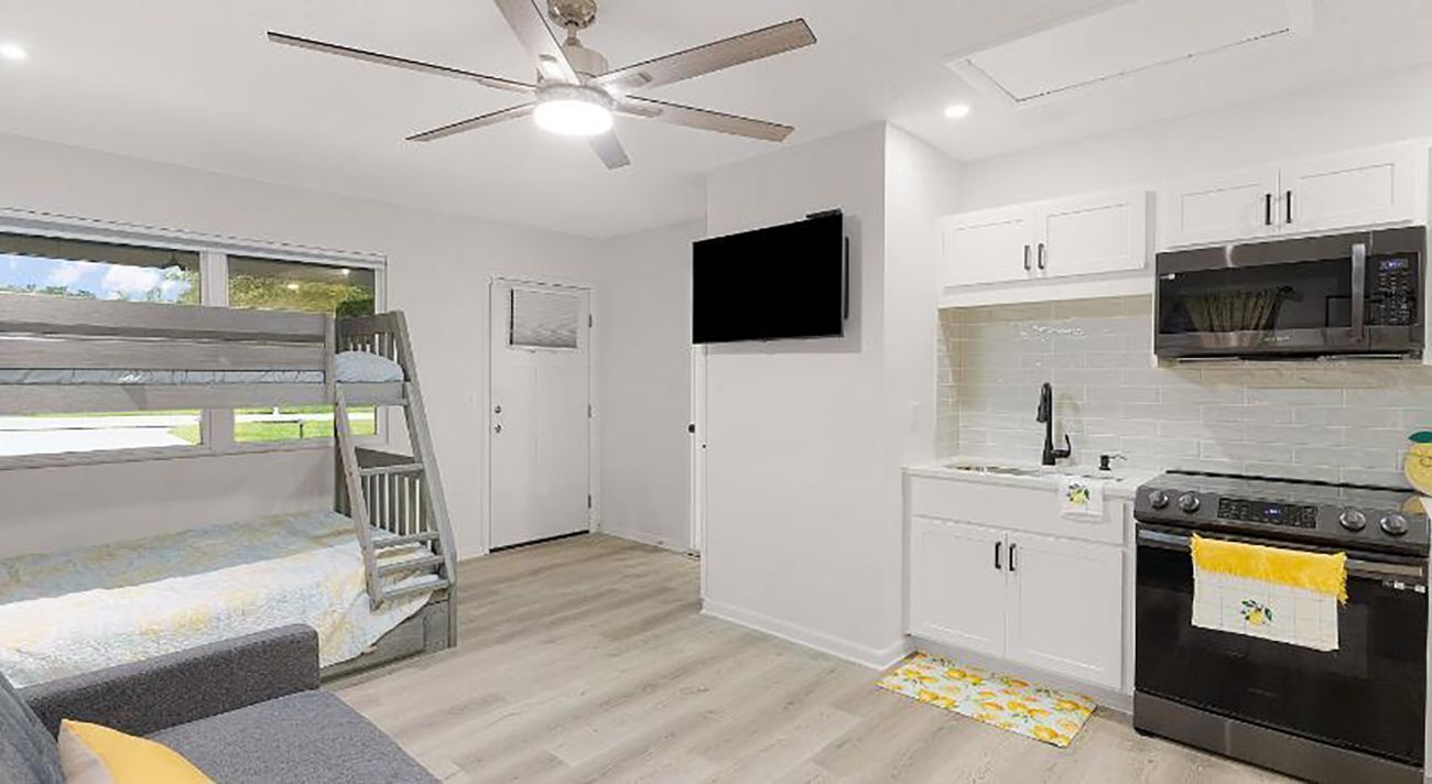 A compact kitchen with white cabinets, a microwave, an oven, and a ceiling fan.