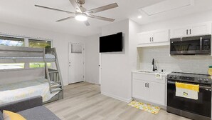 Cozinha compacta com armários brancos, micro-ondas, forno e ventilador de teto.