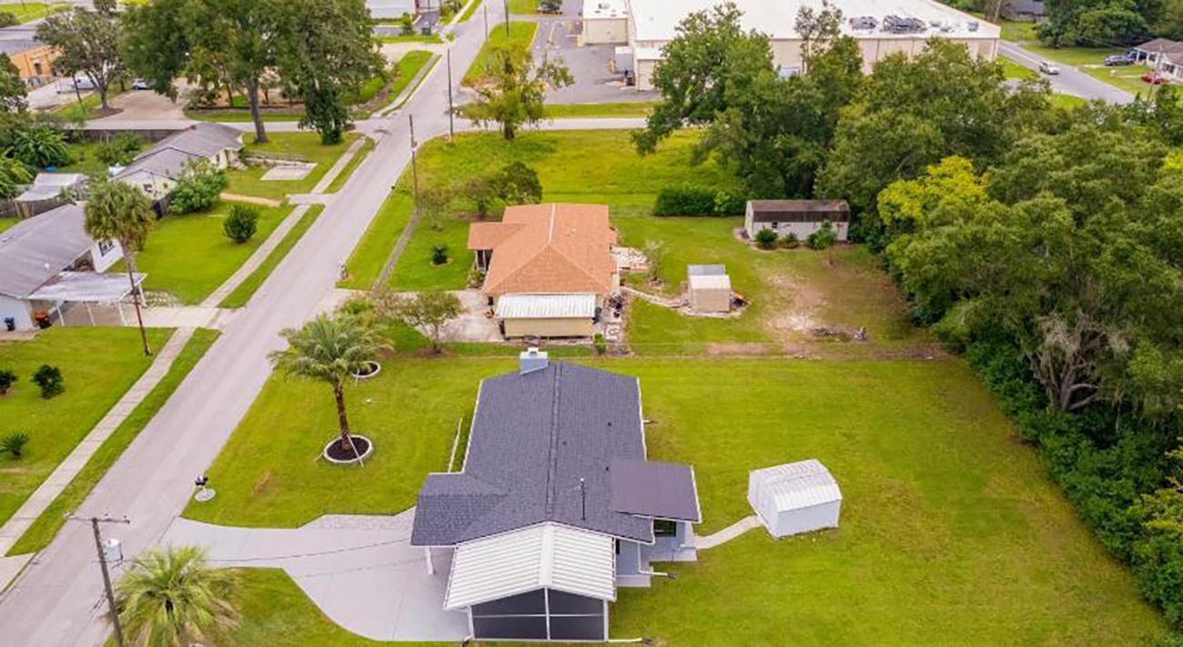 An aerial view of a residential area with a house featuring a sloped roof, a front yard with a small tree, and a driveway leading to the house.