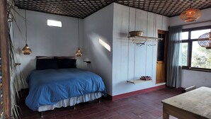 Un dormitorio con cama, luces colgantes, una estantería con una cesta y una ventana con cortinas.
