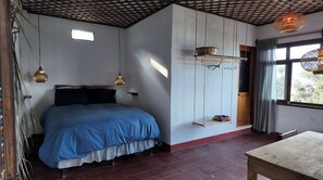 Een slaapkamer met een bed, hangende lampen, een plank met een mand en een raam met gordijnen.