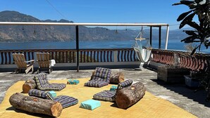 Eine Terrasse mit Sitzgelegenheiten im Freien, einer Hängematte und Blick auf Wasser und Berge.