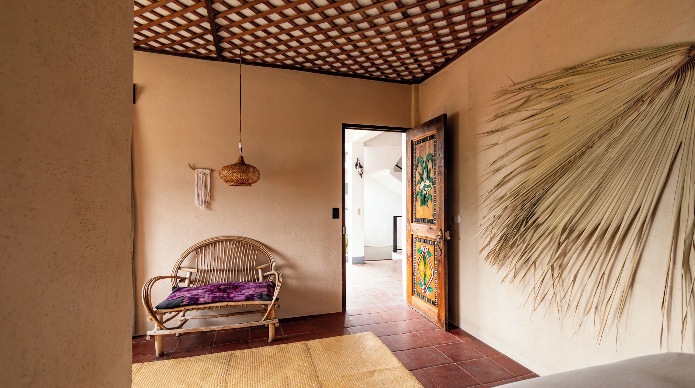 A room with a woven chair, a hanging light fixture, and a door with a decorative panel.