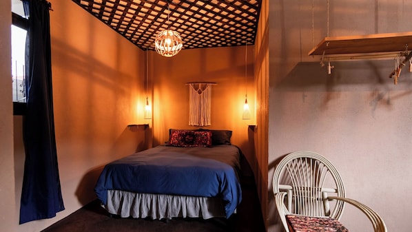 A bedroom with a bed, two wall-mounted lights, a macrame wall hanging, and a chair. - La Cocina Bonita (San Pedro La Laguna)
