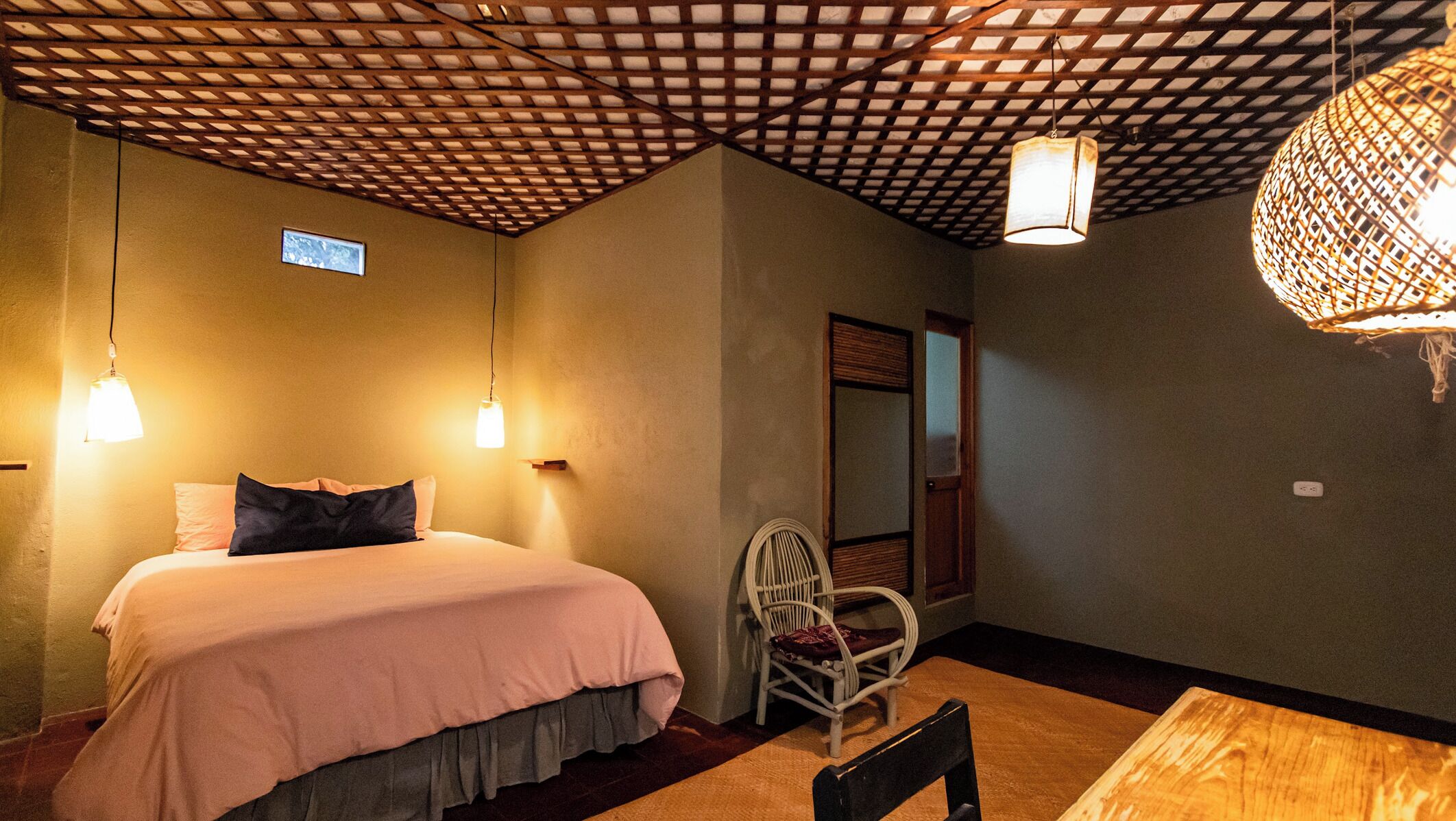 Un dormitorio con una cama, dos luces en la pared, una silla y techo de madera.