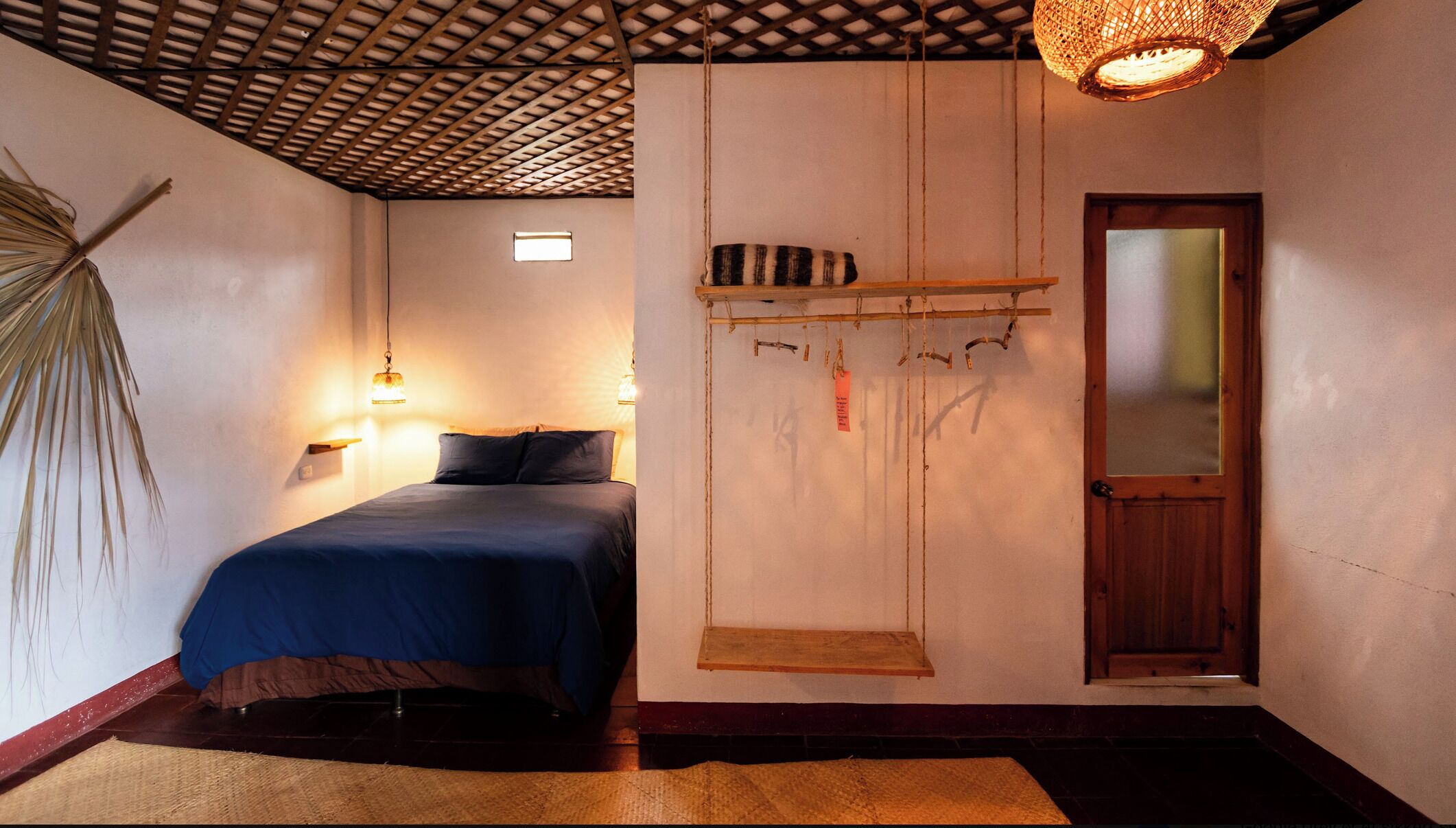 A room with a bed, a hanging swing, a shelf with items, a mirror, and a ceiling fan.