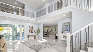 A spacious, multi-level interior with a modern design, featuring a central open area, a dining area, and a staircase with a railing. - Luxe 7BR|Game Room, Firepit & Mini-putt| Sleeps 22 (Fresno)