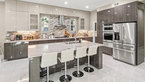 A modern kitchen with a central island, stainless steel appliances, and a sleek design. - Luxe 7BR|Game Room, Firepit & Mini-putt| Sleeps 22 (Fresno)