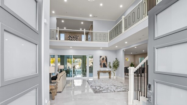 A spacious, modern interior with a polished marble floor, a central seating area with a sofa and table, and a staircase leading to an upper level. - Luxe 7BR|Game Room, Firepit & Mini-putt| Sleeps 22 (Fresno)