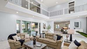 A spacious living area with two beige sofas, a marble coffee table, and a large window overlooking a garden. - Luxe 7BR|Game Room, Firepit & Mini-putt| Sleeps 22 (Fresno)