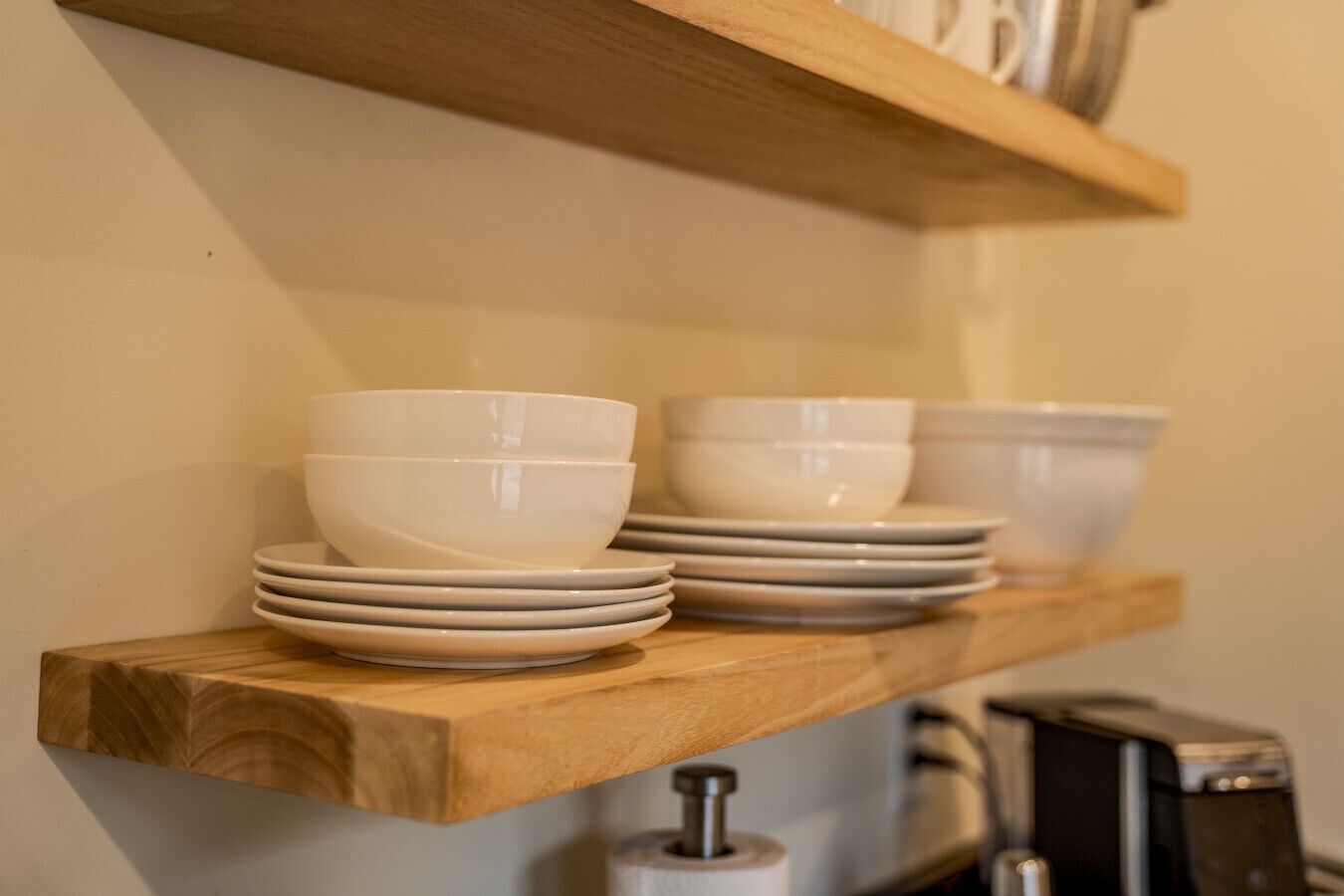 Une étagère en bois sur laquelle sont empilés des bols et des assiettes blancs.