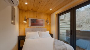 A bedroom with a large bed, wooden walls, an American flag, and a sliding glass door to a deck. - Shipping Container at Double Nickel Farm (Hurricane)