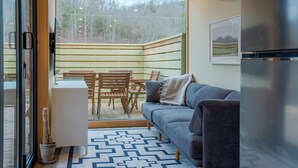 A cozy interior with a wooden ceiling, a grey sofa, a small table, and a chair. - Shipping Container at Double Nickel Farm (Hurricane)