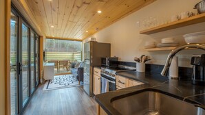 A modern kitchen with a stainless steel sink, wooden cabinets, and a dining area with a table and chairs. - Shipping Container at Double Nickel Farm (Hurricane)