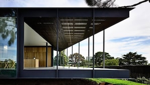 A modern building with a large glass facade, a wooden interior, and a covered outdoor area with seating.