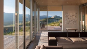 A modern living room with a large glass wall, a sofa, a table, and a chair.