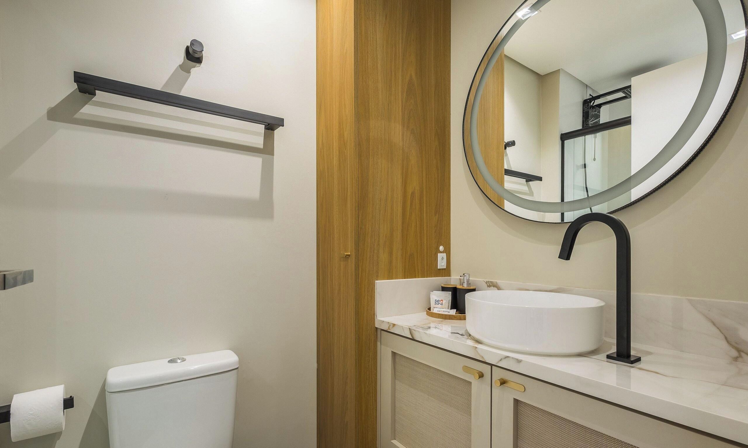 Un baño con inodoro, lavamanos con espejo y un perchero para toallas.