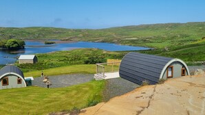 A rural landscape with a small lake, two dome-shaped cabins, and a grassy area with a wooden deck.