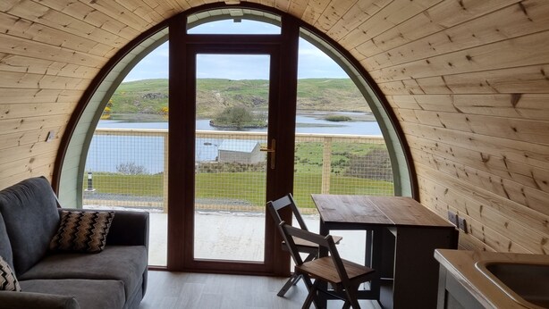 A cozy room with a wooden interior, a sofa, a table, and a view of a lake and hills.