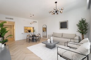 A modern living room with a sofa, coffee table, and dining area. - Stayshort - Luxury 1 Bedroom in Downtown With Burj Khalifa View (Dubai)