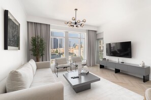 A modern living room with a sofa, chairs, a coffee table, a TV, and a city view through large windows. - Stayshort - Luxury 1 Bedroom in Downtown With Burj Khalifa View (Dubai)
