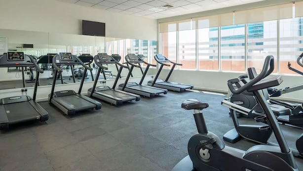 A gym with multiple treadmills and exercise bikes, large windows, and a tiled floor. - Stayshort - Peaceful Studio in Production City That Sleeps 3 (Dubai)