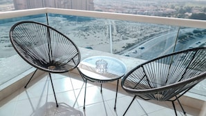 A balcony with two black wire chairs and a glass table, overlooking a cityscape with buildings and roads. - Stayshort - Peaceful Studio in Production City That Sleeps 3 (Dubai)