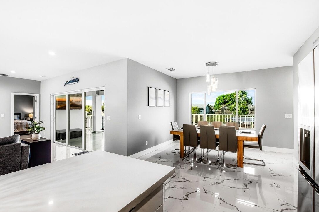 A modern kitchen with a marble countertop, a dining area with a table and chairs, and a view of greenery outside.