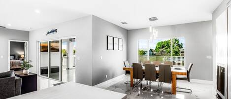 A modern kitchen with a marble countertop, a dining area with a table and chairs, and a view of greenery outside.