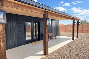 A modern building with a covered patio area, wooden beams, and a gravel ground. - Cozy Western Cowboy Cottage in Kanab, Fire pit, Close to Zion National Park (Kanab)