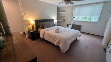 A bedroom with a bed, nightstand, lamp, ceiling fan, and a window with blinds.