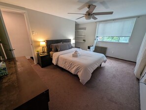 A bedroom with a bed, nightstand, lamp, ceiling fan, and a window with blinds.