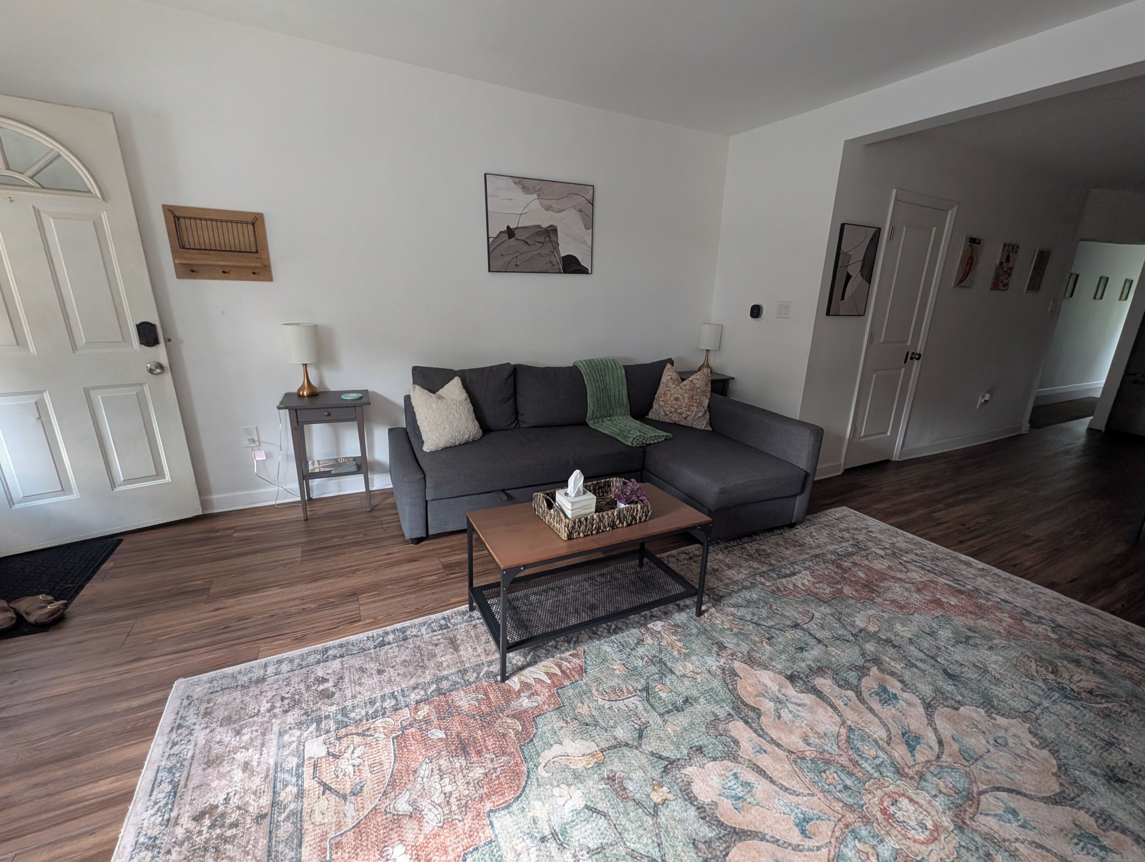 A living room with a grey sofa, a coffee table, a patterned rug, and a door with a white frame.