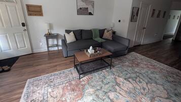 A living room with a grey sofa, a coffee table, a patterned rug, and a door with a white frame.