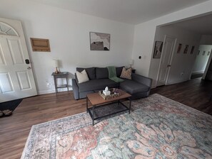 A living room with a grey sofa, a coffee table, a patterned rug, and a door with a white frame.