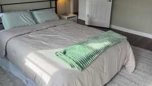 A neatly made bed with a patterned bedspread and a green throw blanket, a bedside lamp, and a white door in a room with a simple, clean design.