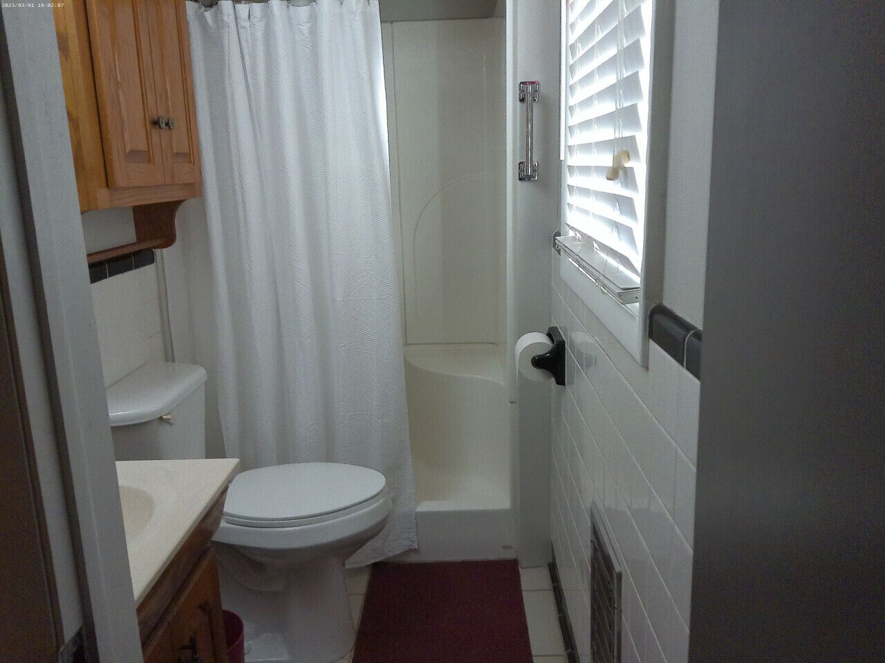 Un baño pequeño con inodoro, ducha y ventana con persianas.