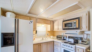 A compact kitchen with a refrigerator, microwave, toaster, kettle, and stove. - #84 Tiger Run (Breckenridge)