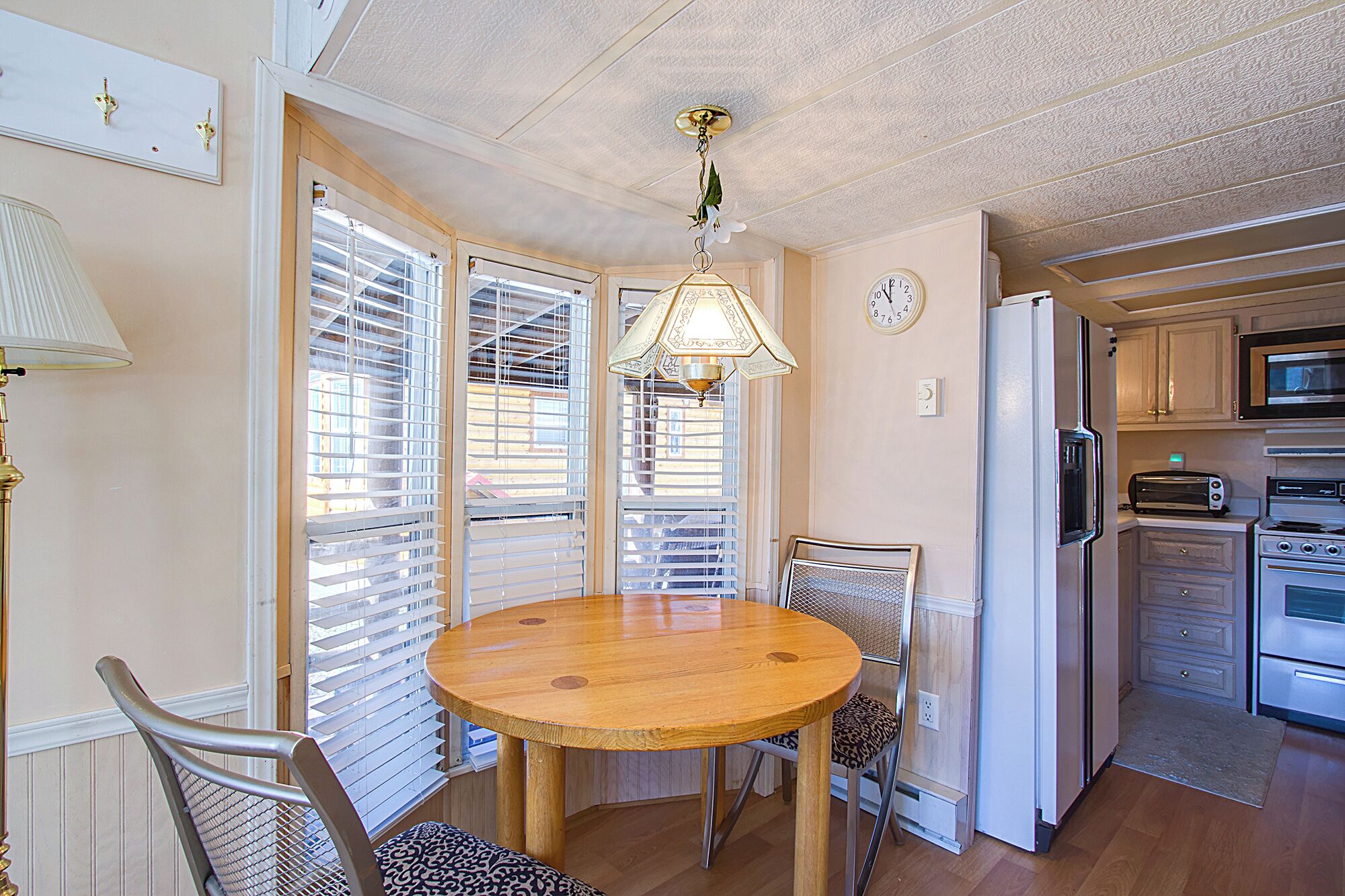 Un coin repas comprenant une table ronde en bois, des chaises, un luminaire suspendu et une cuisine équipée.