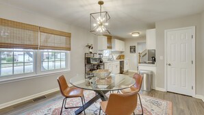 Un coin repas avec une table en verre, des fauteuils en cuir, un panier tressé et un lustre moderne.