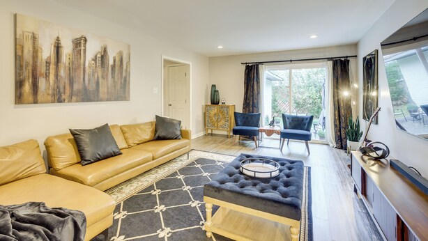 Un salon moderne avec un canapé, un pouf et un tableau représentant un paysage urbain.