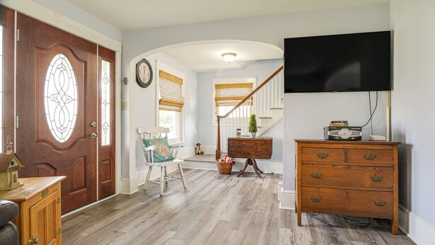 A hallway with a wooden door, a white chair, a wooden dresser, and a television mounted on the wall. - Close to Venues & Fairgrounds! York Area Home (Red Lion)