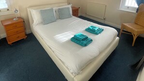 Ein Schlafzimmer mit einem Bett, Nachttischen, einem Sessel, einem Heizkörper, einem Fenster und einer Pendelleuchte.