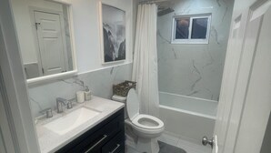 A bathroom with a white sink, vanity, and toilet. There is a shower curtain, a window, and a mirror above the sink.